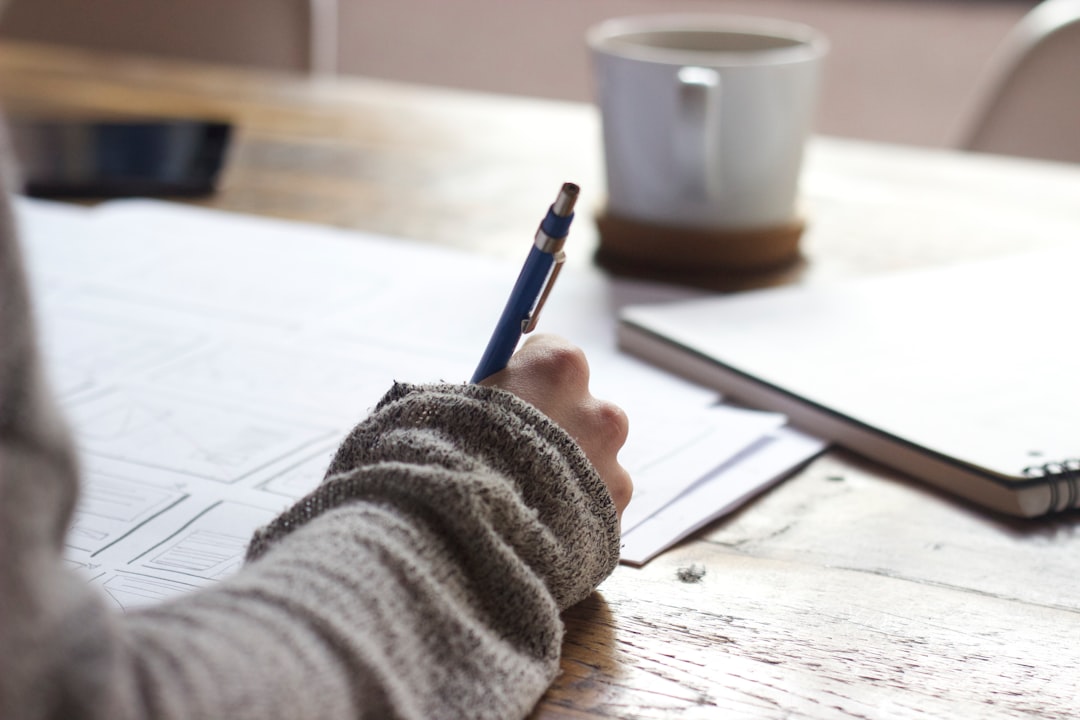 Person writing notes on a wooden table — representing the self-study narrative writing process