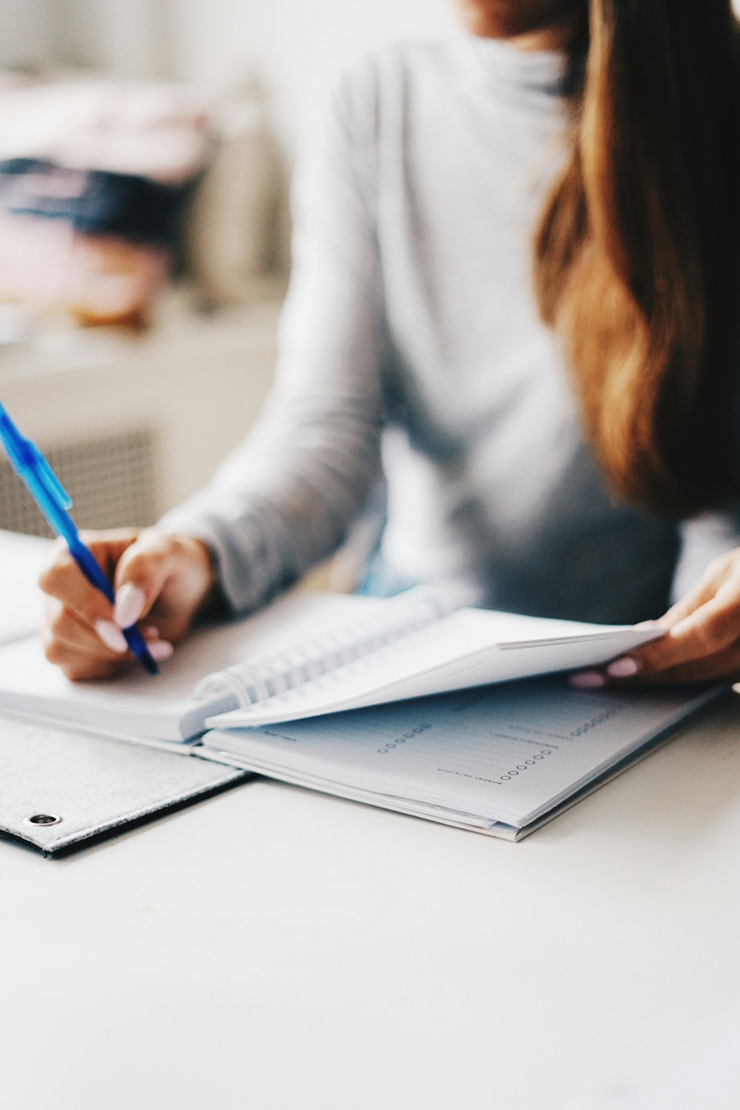 A close-up of a person writing in a notebook with a pen, representing the coordinator drafting the narrative section by section