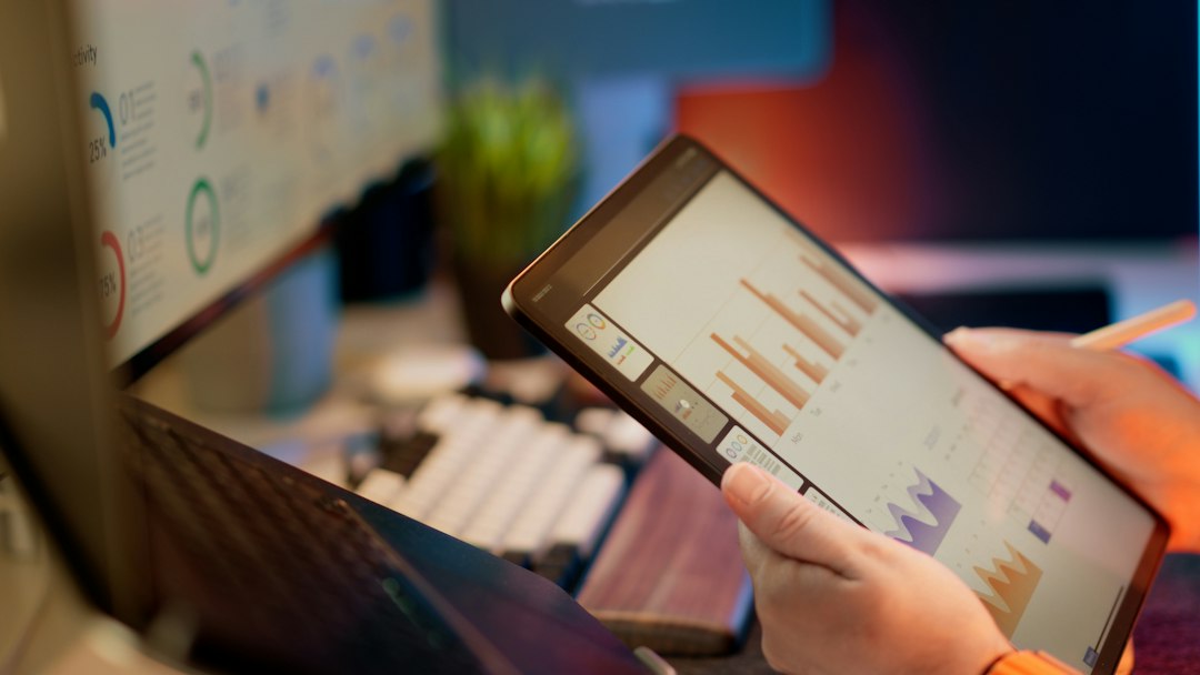Tablet showing a bar-chart analytics dashboard over a laptop, illustrating the relational data models that make continuous review possible