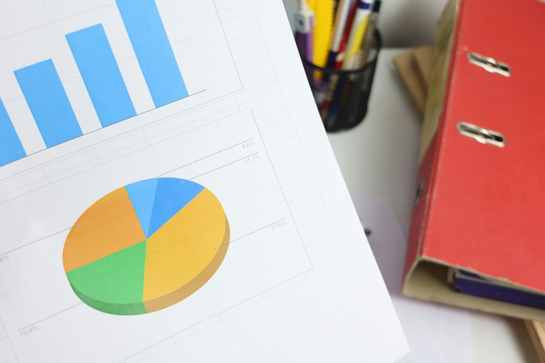 A printed data summary page showing a bar chart and pie chart beside a red binder on a desk