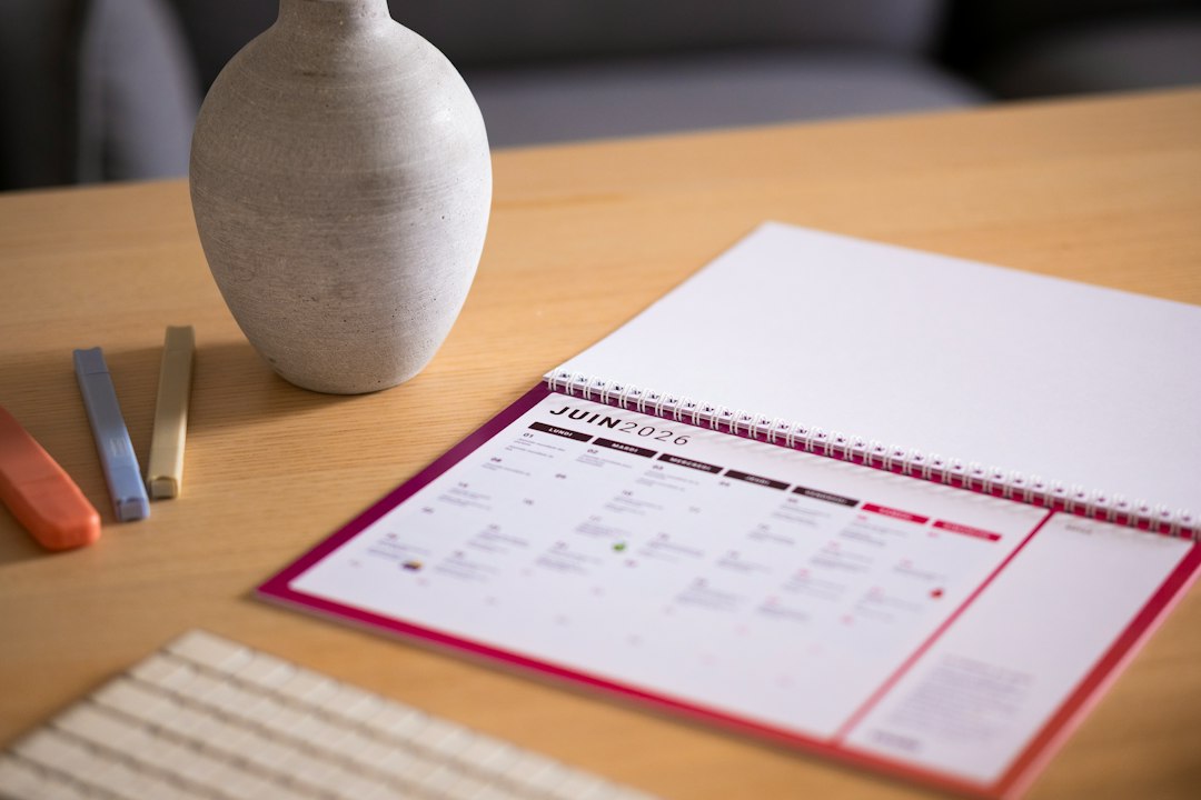 A red-edged desk calendar sits on a wooden table beside a ceramic vase and a keyboard