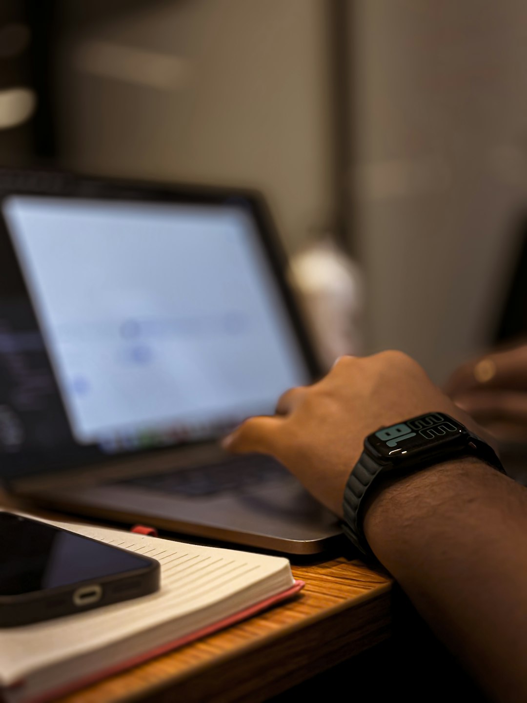 Coordinator's hands typing on a laptop beside a notebook and phone on a wooden desk, illustrating weighing the three decision questions