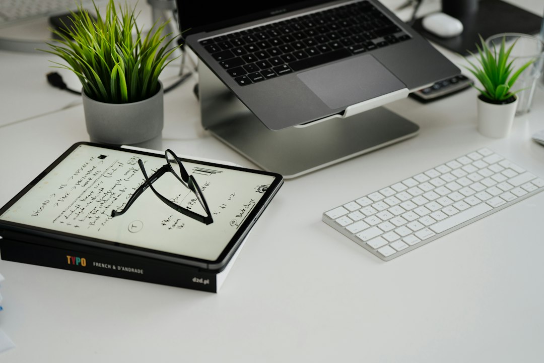 A clean, organized desk with an open laptop, keyboard, reading glasses, and a small potted plant